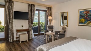 Una habitación de hotel con una cama, un escritorio con lámpara, dos sillas, un televisor y un ventanal con cortinas.