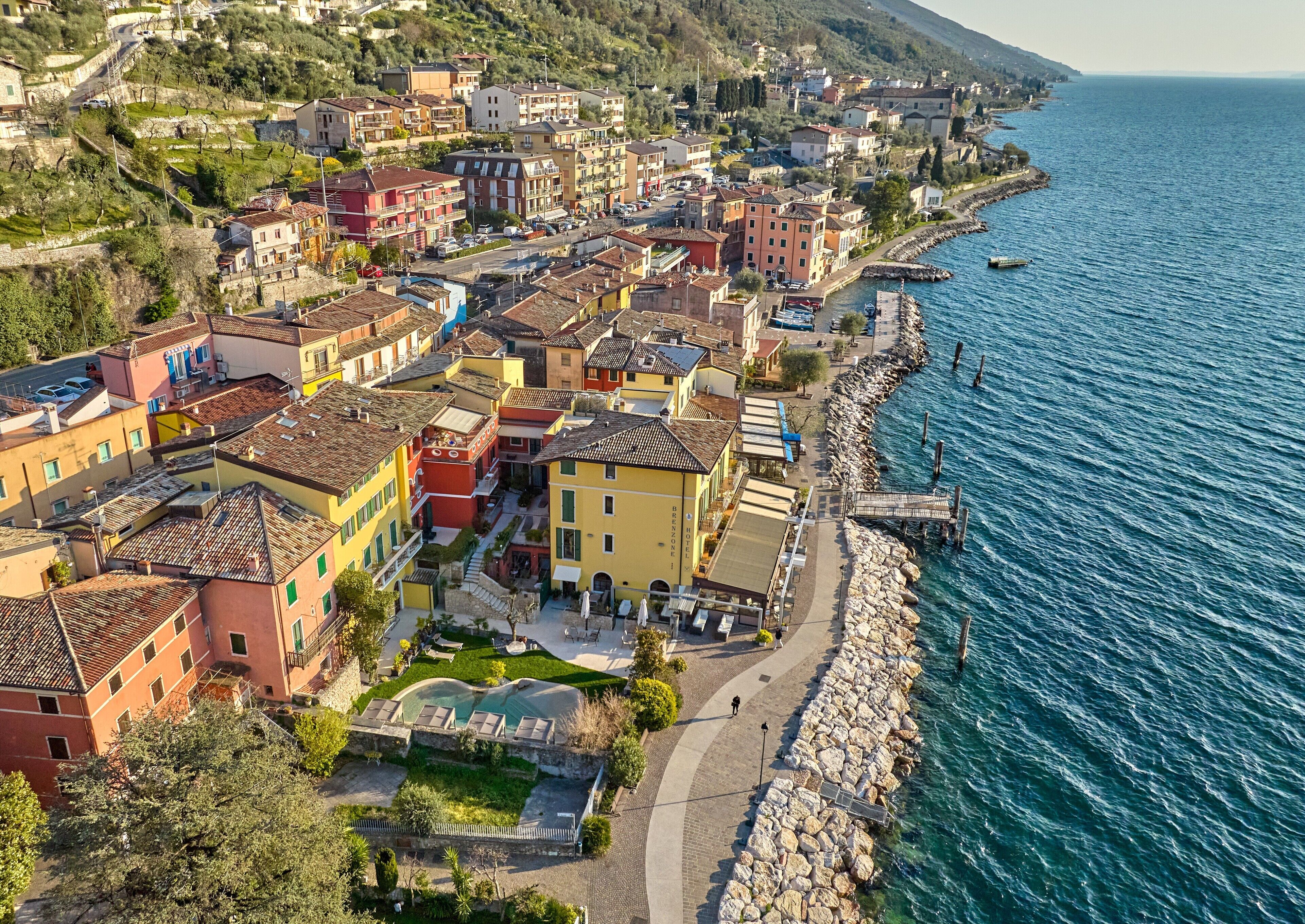A coastal town with colorful buildings, a paved walkway along the sea, and a rocky breakwater.