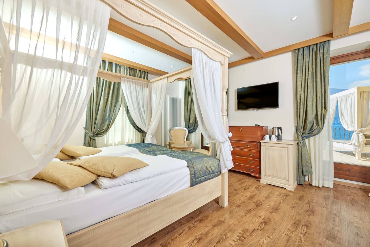 Una cama con dosel, cortinas blancas y verdes, un aparador de madera y un televisor en la pared.