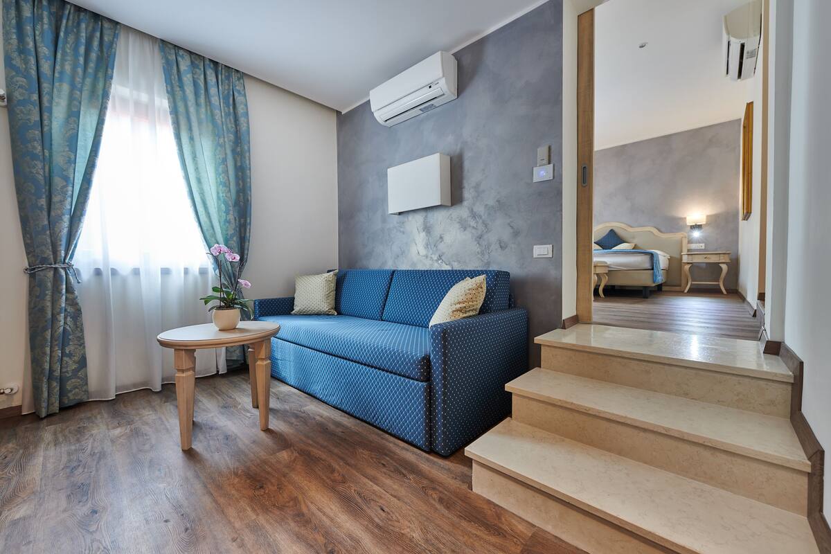 Un moderno salón con un sofá azul, suelo de madera y una escalera que conduce a otra habitación.