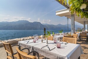 An outdoor dining area with tables set for two, overlooking a body of water and mountains. - Lake Front Hotel Brenzone (Brenzone sul Garda)
