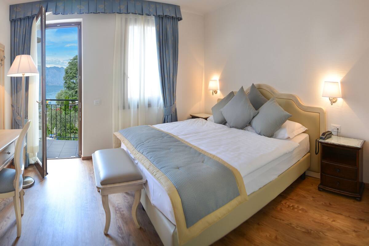 Una habitación de hotel con cama, mesita de noche, lámpara y un escritorio con silla.