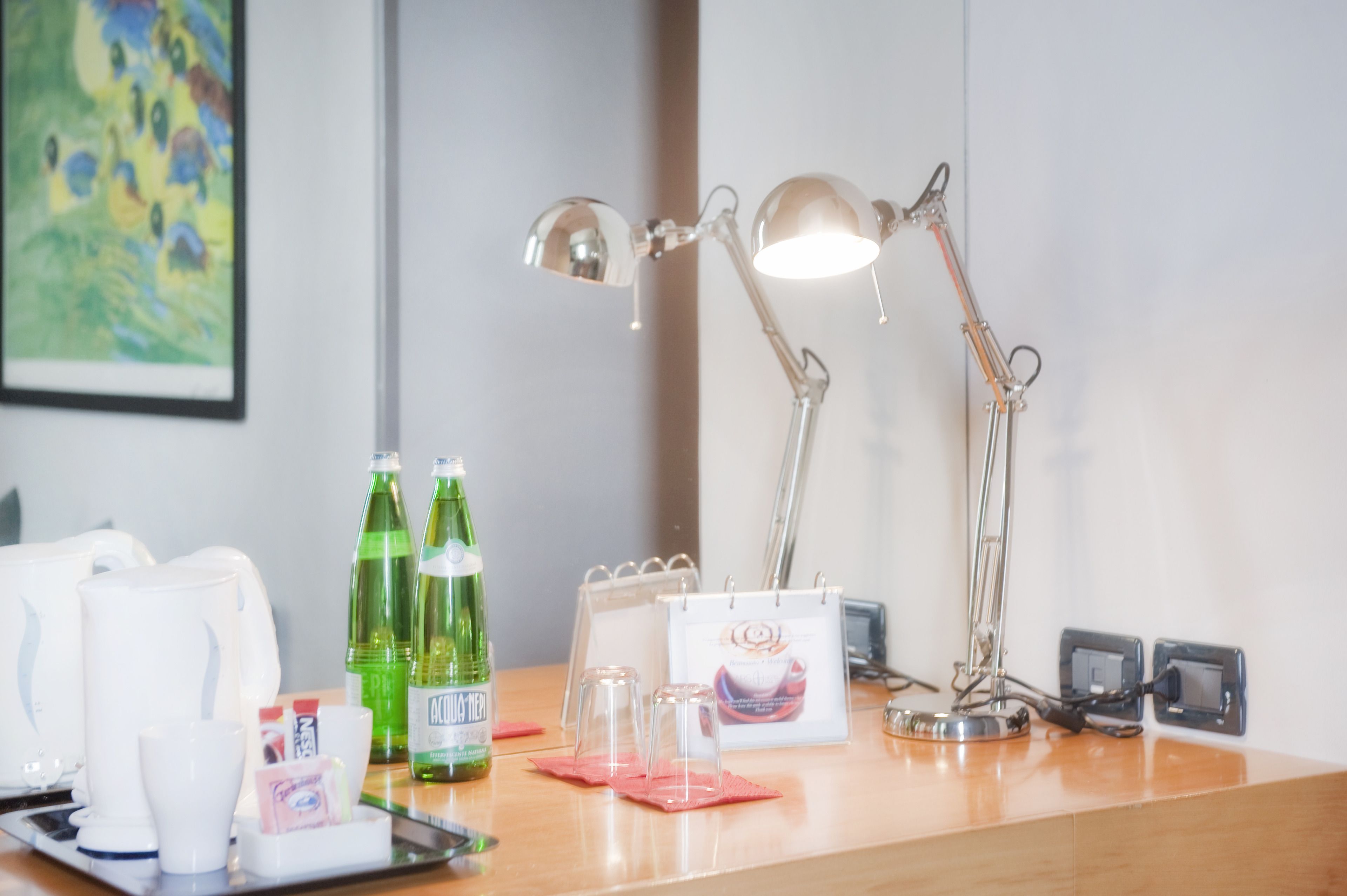 A hotel reception desk with a desk lamp, a calendar, a coffee machine, and two bottles of water.