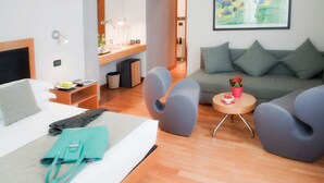 A modern hotel room with a bed, a desk with a lamp, a sofa, and a small table with a flower vase. - Best Western Ars Hotel (Rome)
