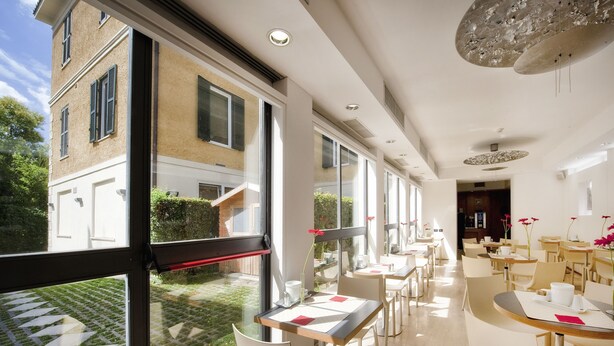 A modern dining area with large windows, a garden view, and a mix of wooden and white furniture. - Best Western Ars Hotel (Rome)