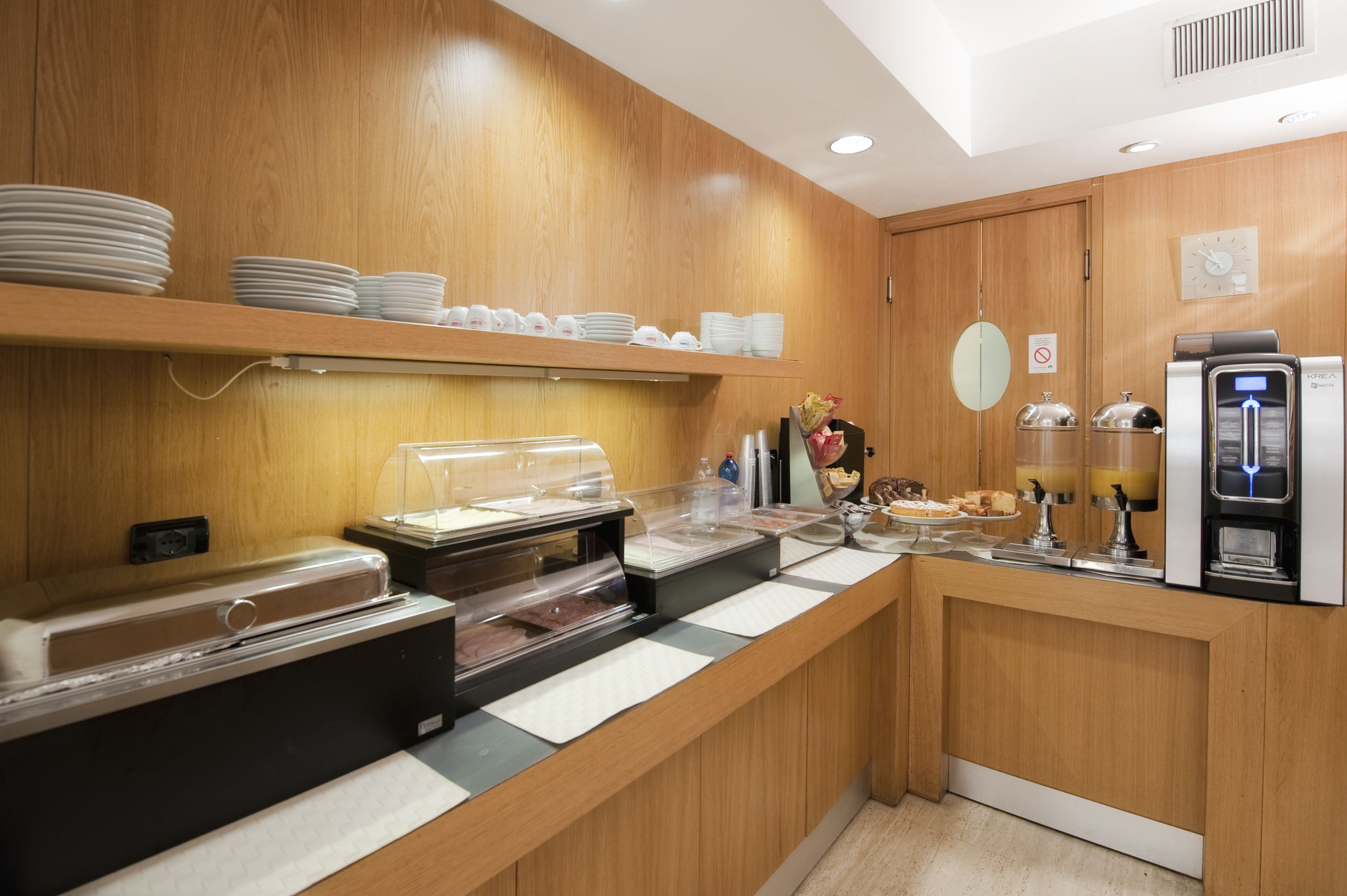 Uma área de buffet com diversas opções de comida, uma máquina de café e um relógio na parede.