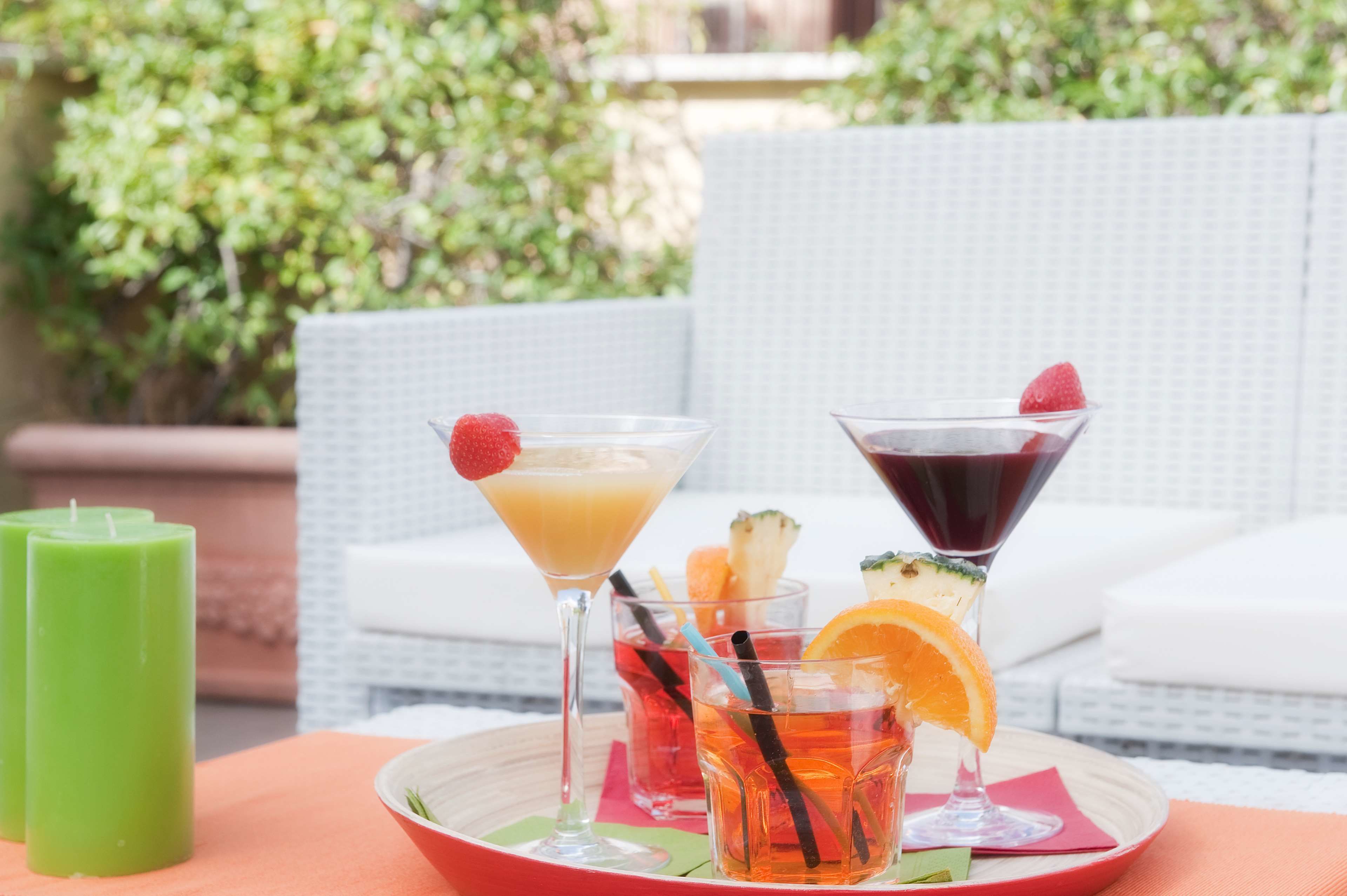 Une table avec trois boissons, une bougie verte et une chaise en osier, le tout dans un décor de jardin.