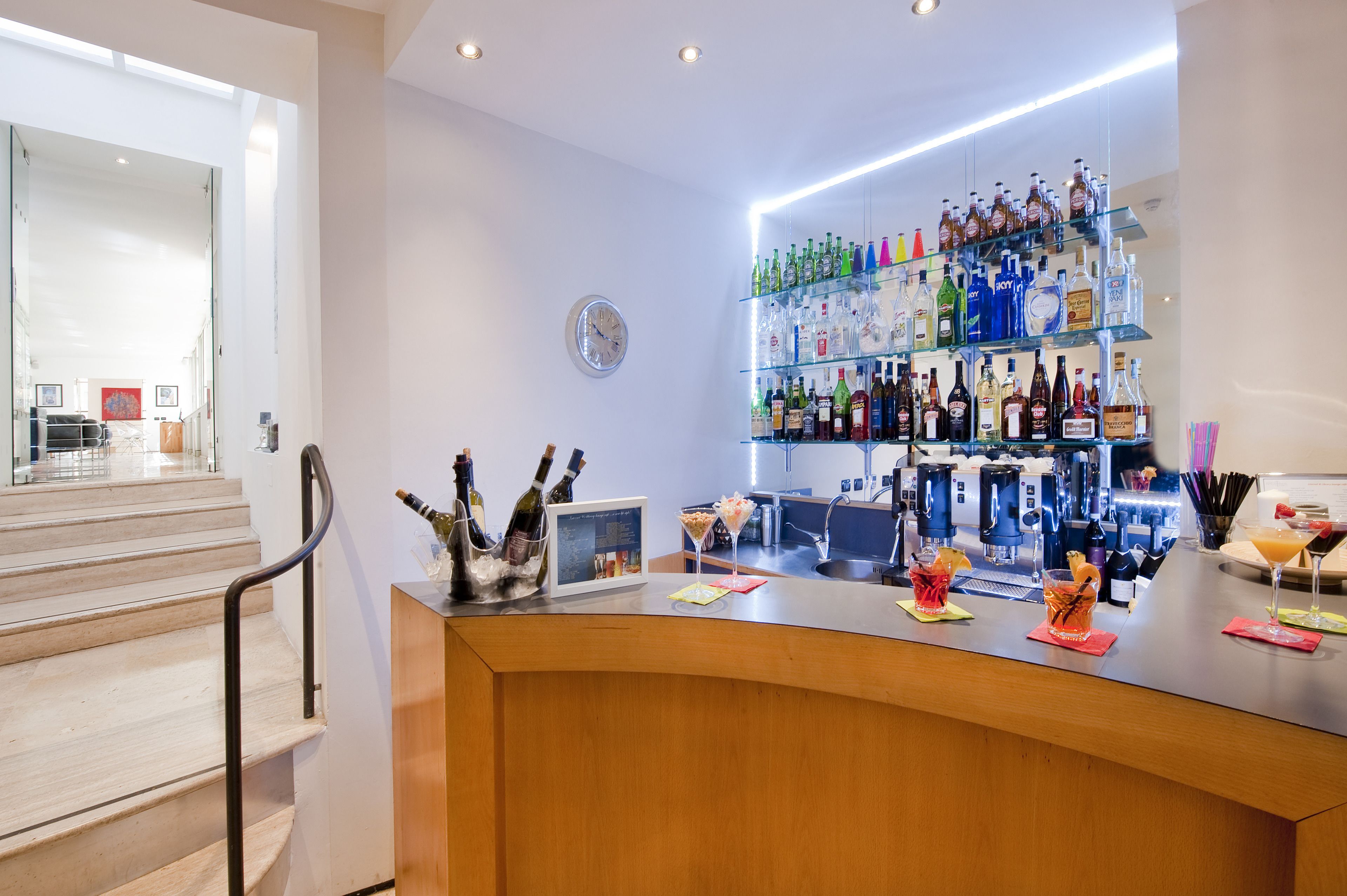 Zona de bar con barra, estantes llenos de botellas de licor y un reloj en la pared.