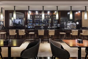 A bar area with multiple seating options, a variety of liquor bottles, and a coffee machine. - Elba Madrid Alcalá (Madrid)