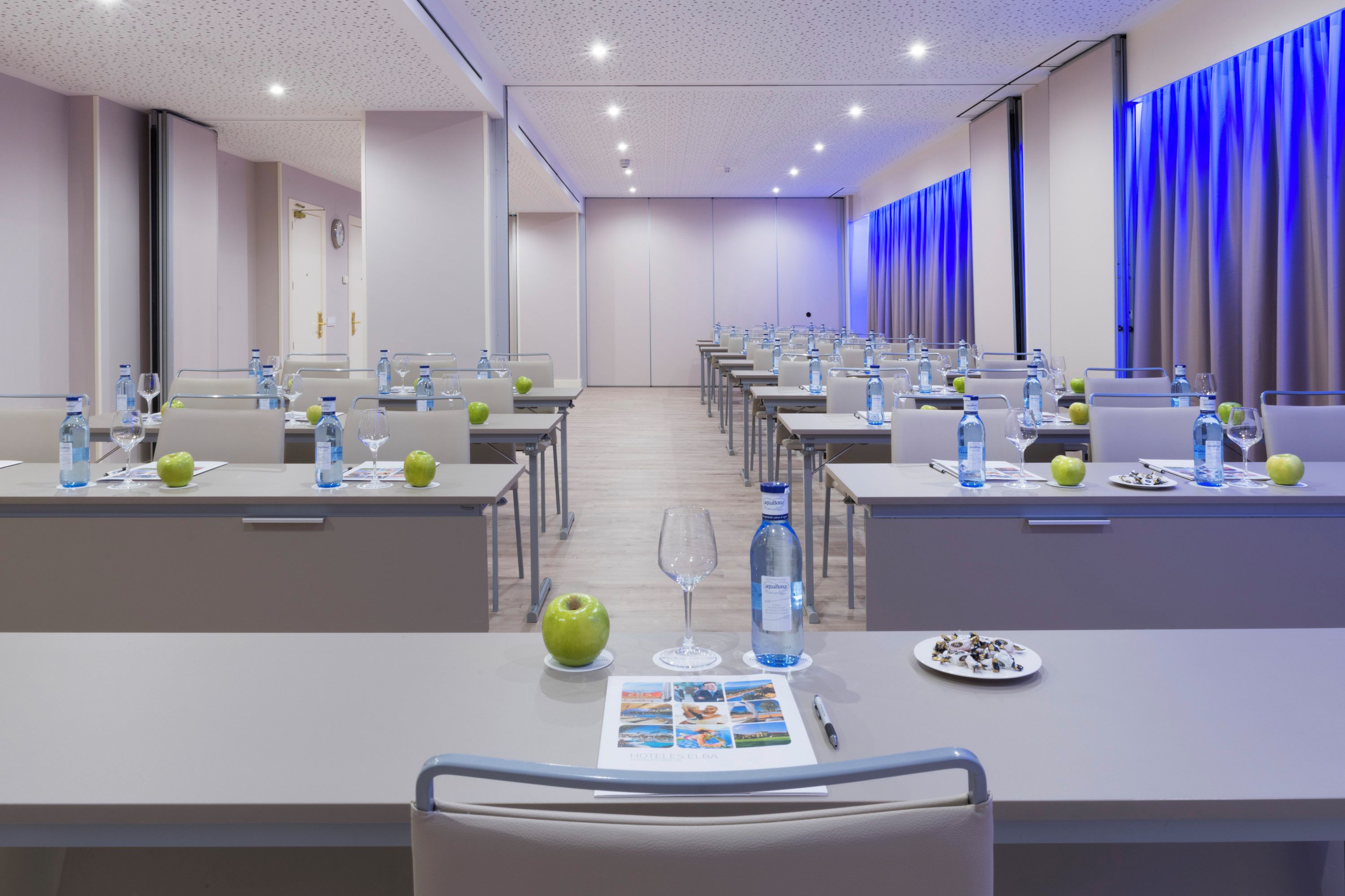 A conference room with tables set for a meeting, equipped with water bottles, glasses, and apples.