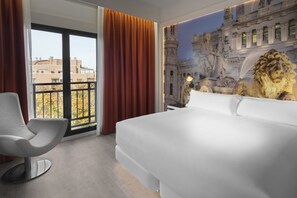 A hotel room with a large bed, a modern chair, a view of buildings, and a mural of a lion. - Elba Madrid Alcalá (Madrid)