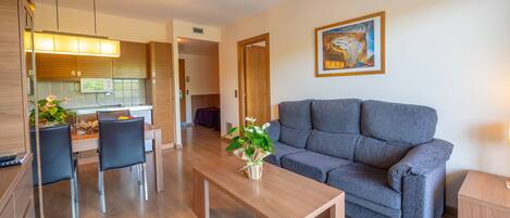 A modern living room with a grey sofa, wooden coffee table, and a dining area with a wooden table and chairs.