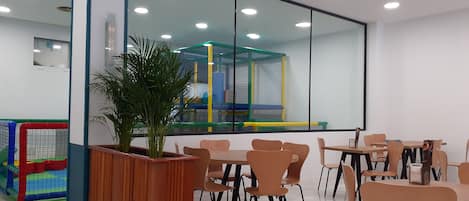Un espacio interior moderno con una zona de juegos, varias mesas y sillas, y un espejo grande que refleja la habitación.