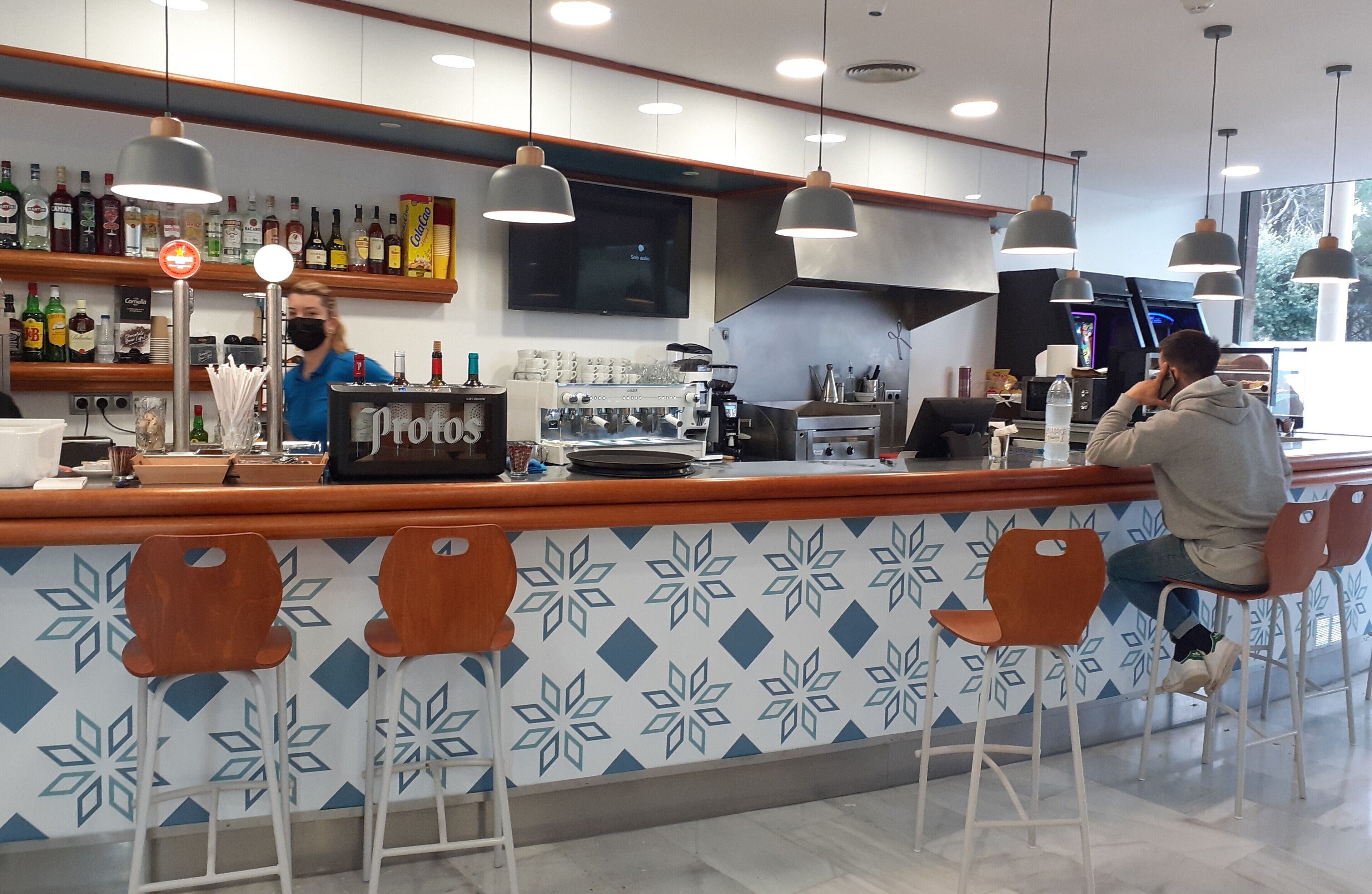 Un'area bar moderna con un pannello decorativo, sgabelli da bar e diverse bottiglie di liquori sugli scaffali.