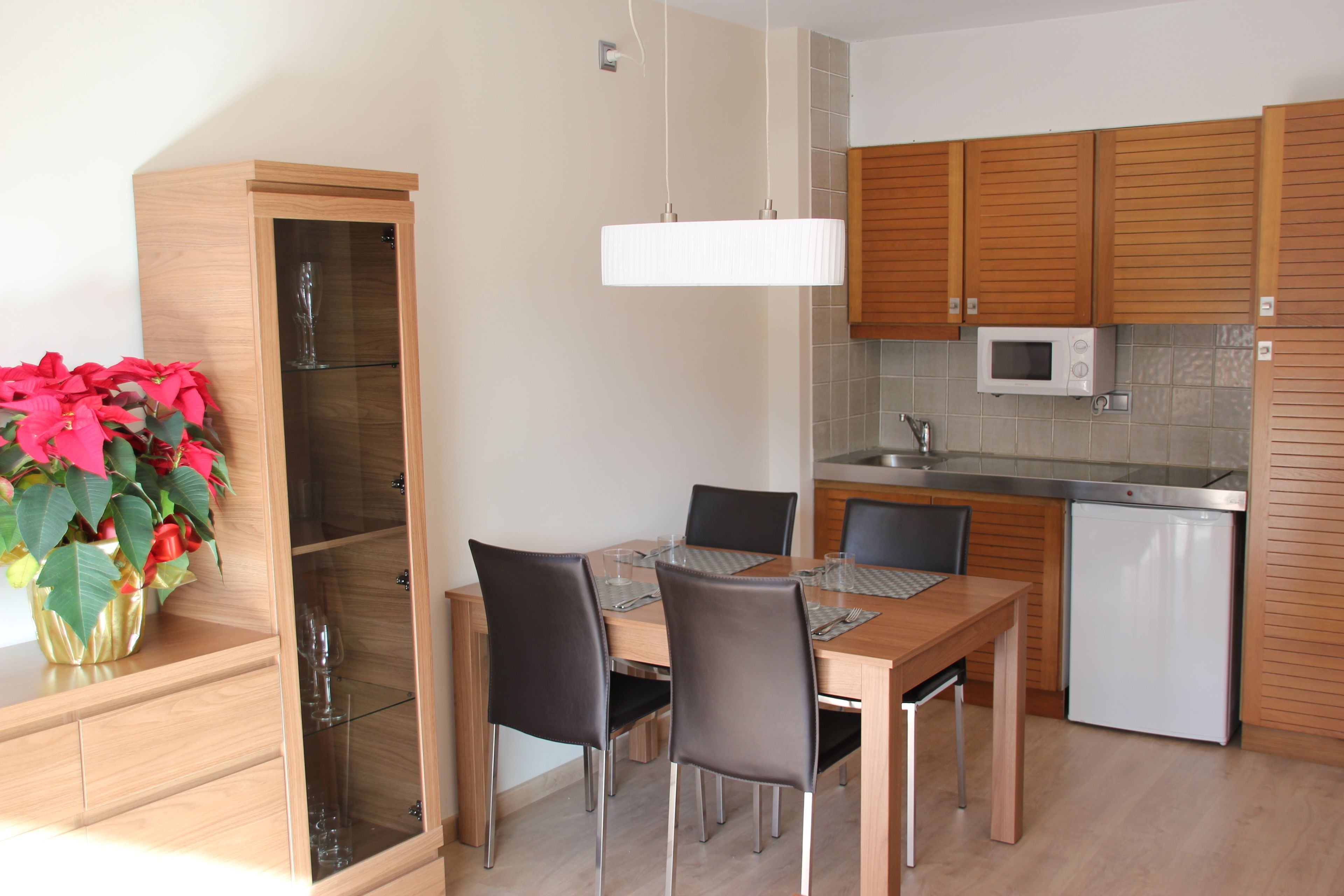 A modern kitchen with wooden cabinets, a built-in microwave, and a dining area with a wooden table and chairs.