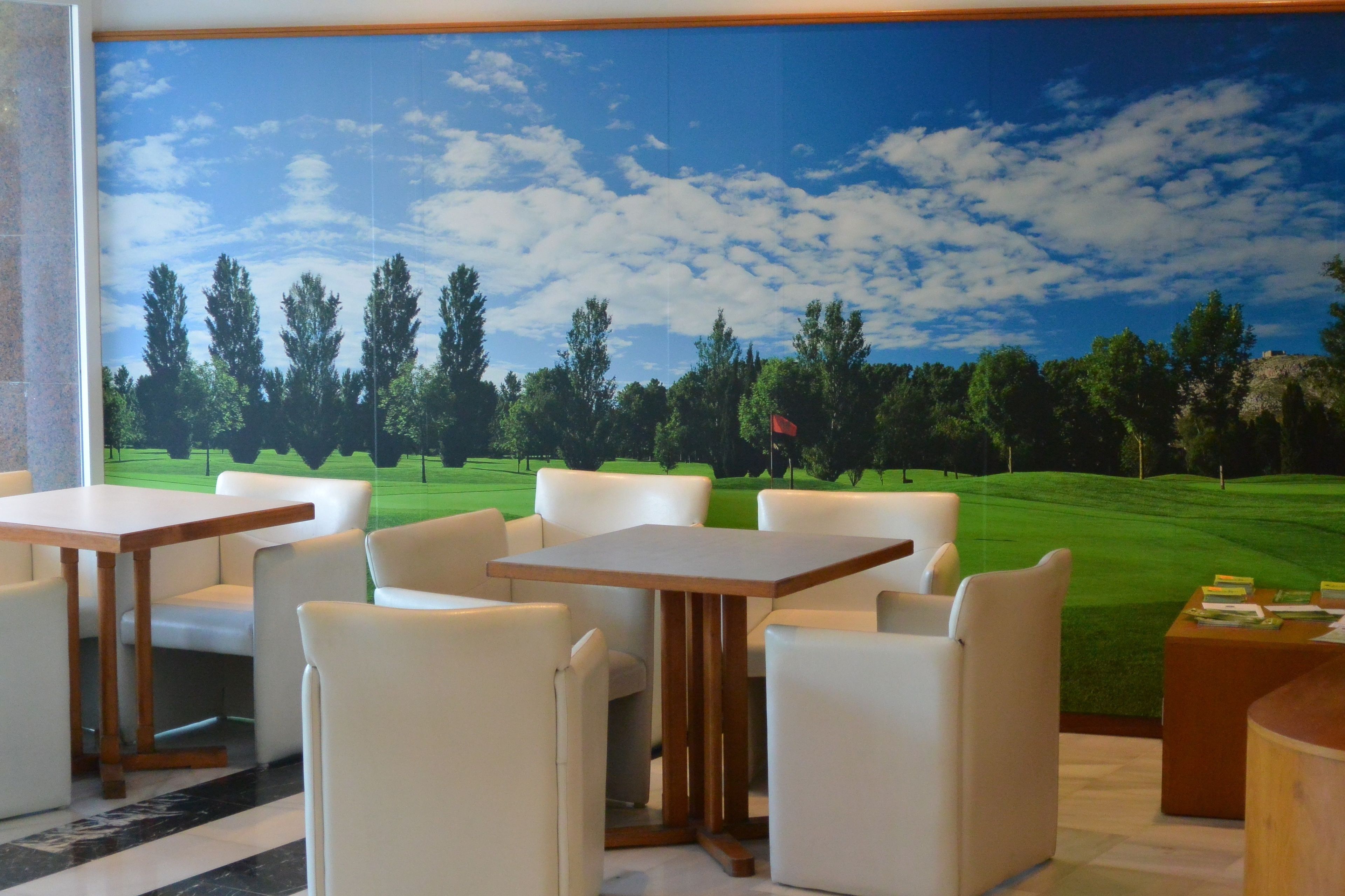 Una stanza con un grande murale che raffigura un campo da golf, poltrone in pelle bianca e un tavolo di legno.