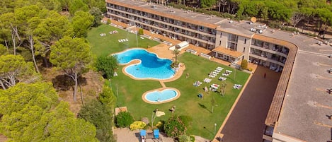 An aerial view of a hotel with a swimming pool, multiple balconies, and a surrounding landscape.
