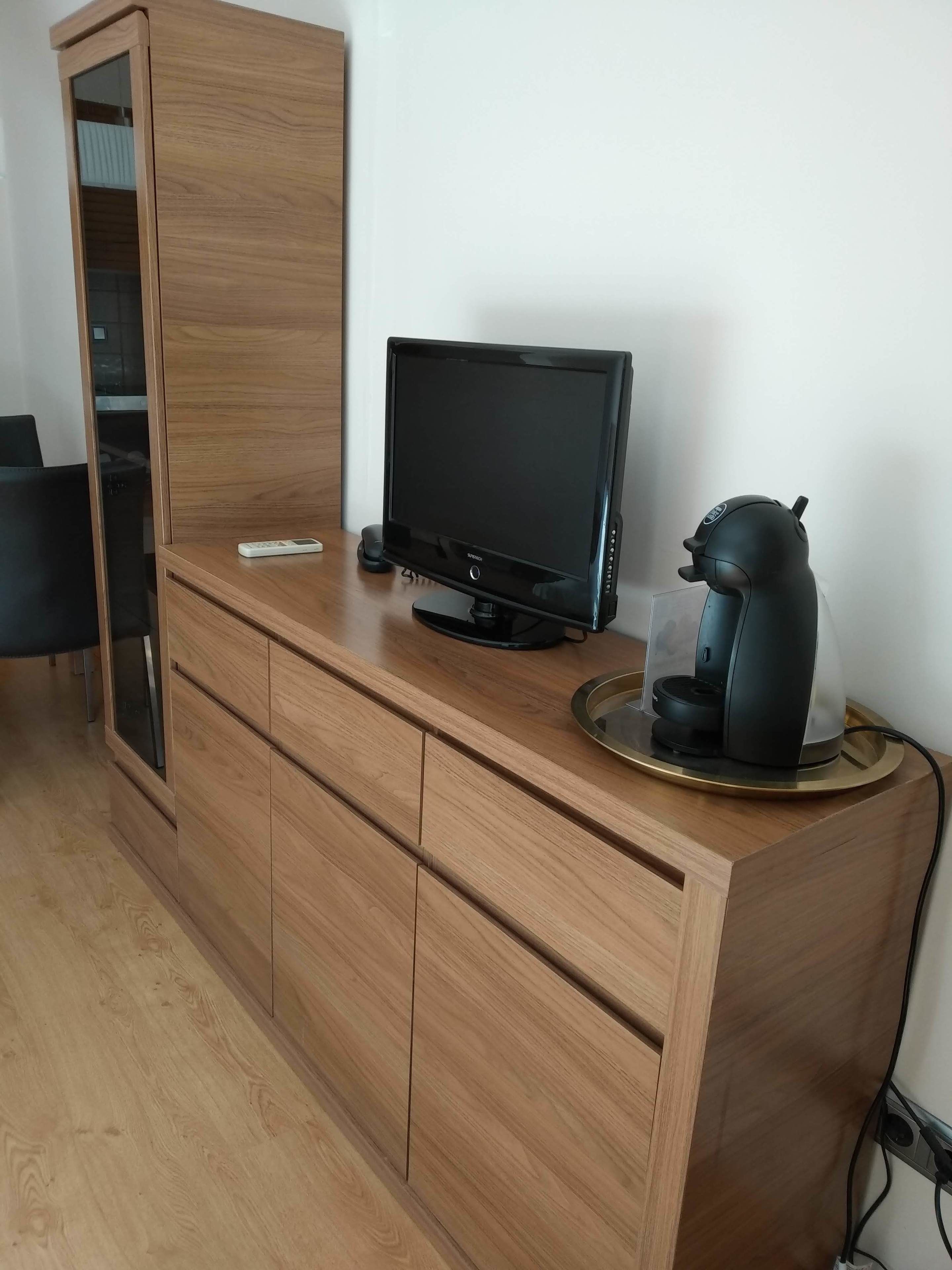 A wooden cabinet with a flat-screen TV, a coffee maker, and a scale on top.