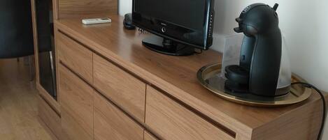 Een houten kast met een flatscreen-tv, een koffiezetapparaat en een weegschaal erboven.