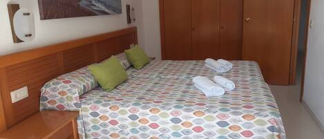 A bedroom with a bed, two pillows, a wooden nightstand, a wooden wardrobe, and a painting of a beach scene on the wall.