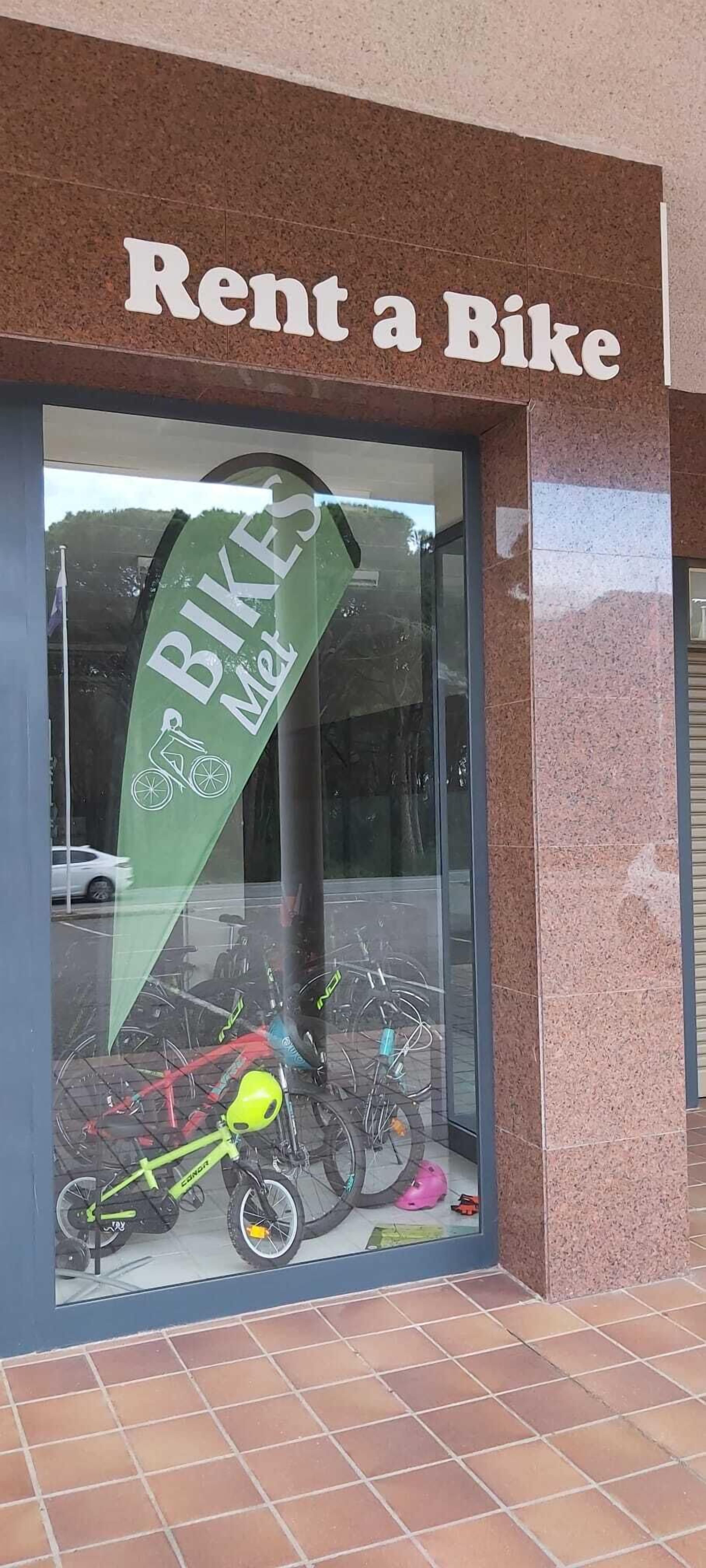 Una tienda con un letrero que dice “Alquila una bicicleta” y un cartel anunciando “Bicicletas Met.”