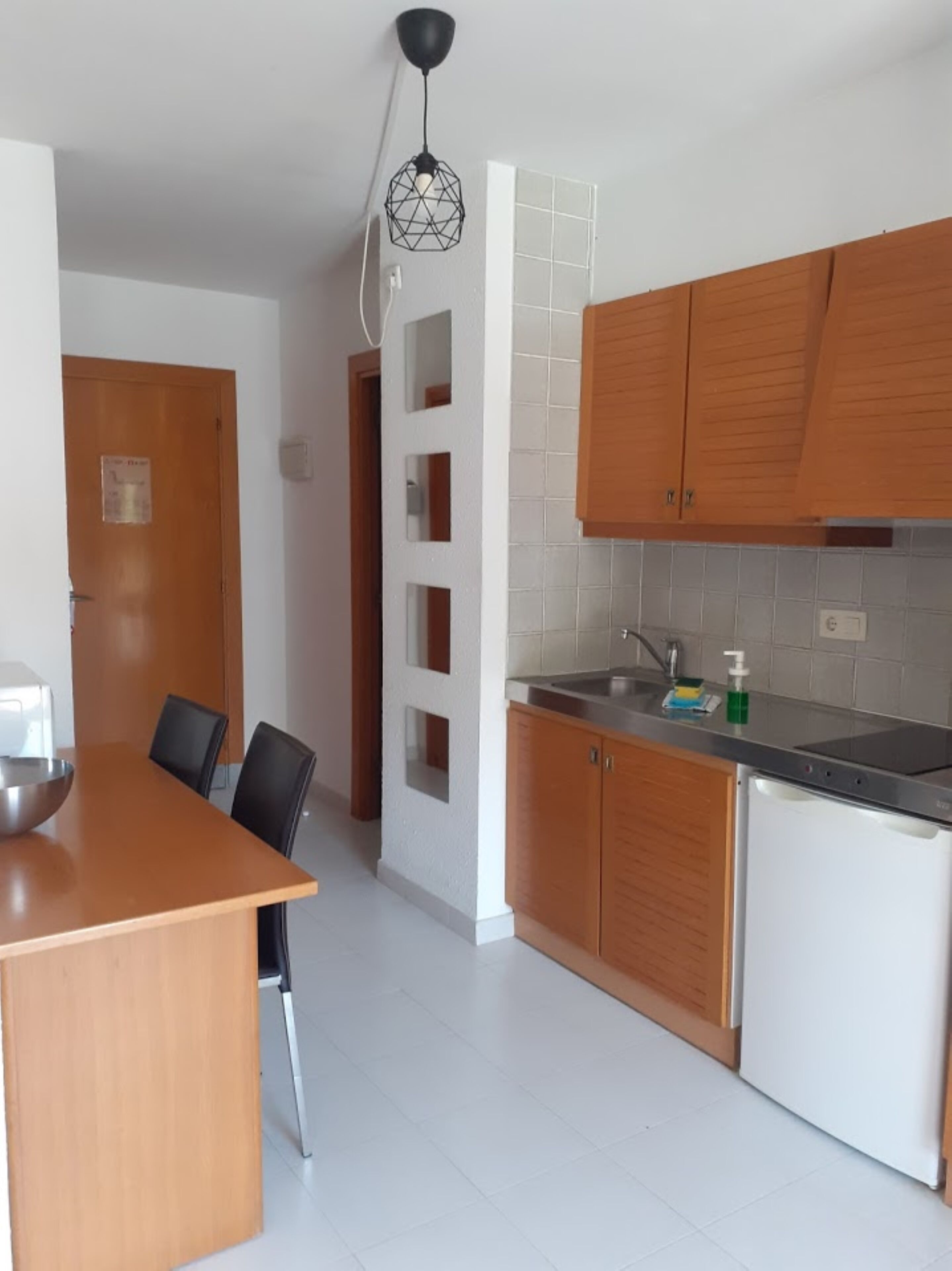 Una cocina moderna con armarios de madera, salpicadero de azulejos blancos y un lavamanos de acero inoxidable.