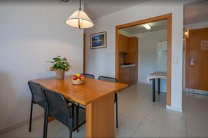 Cozy dining area with a wooden table and four chairs, featuring a potted plant and a fruit basket.