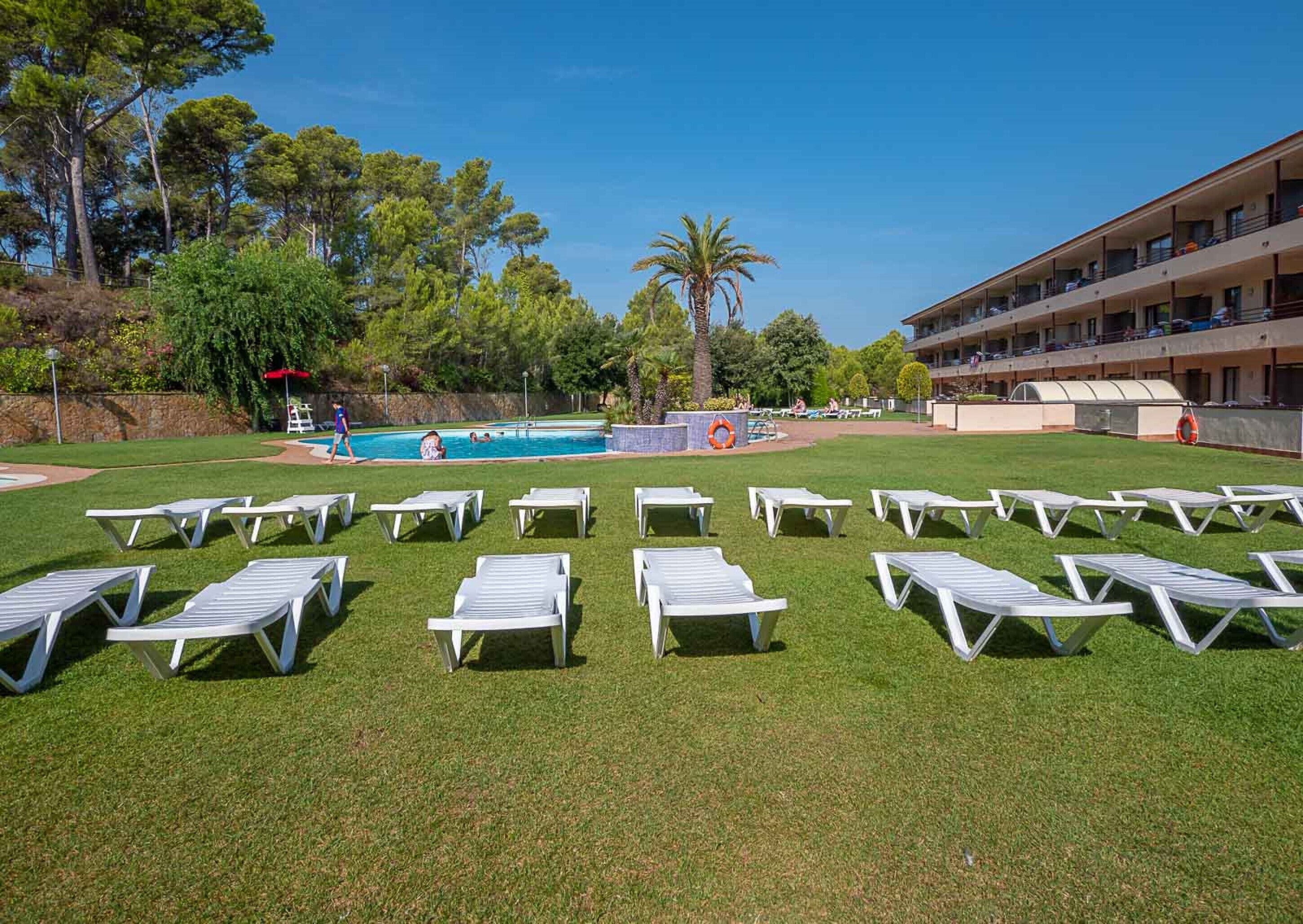 A pool area with white lounge chairs, a swimming pool, and a building with balconies.