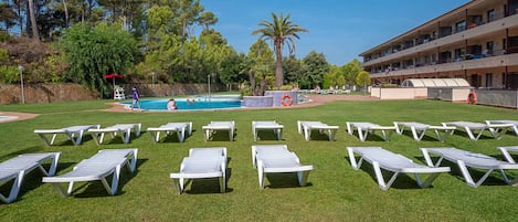 A pool area with white lounge chairs, a swimming pool, and a building with balconies.