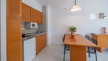 Cocina compacta con armarios de madera, microondas y comedor con mesa y sillas.
