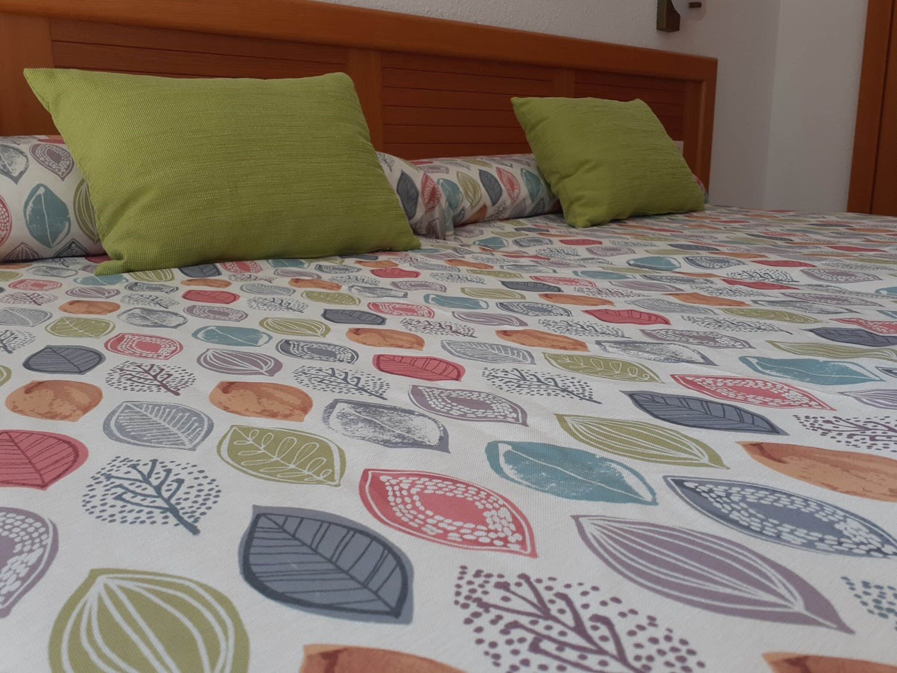Een bed met een beddegoed met een patroon en twee groene kussens.
