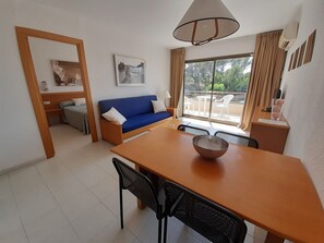 Relax in this serene space with a sofa, dining table, and large window offering a view of lush greenery.