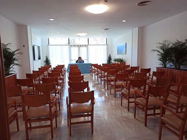 A conference room with rows of wooden chairs facing a blue table where a person is seated.
