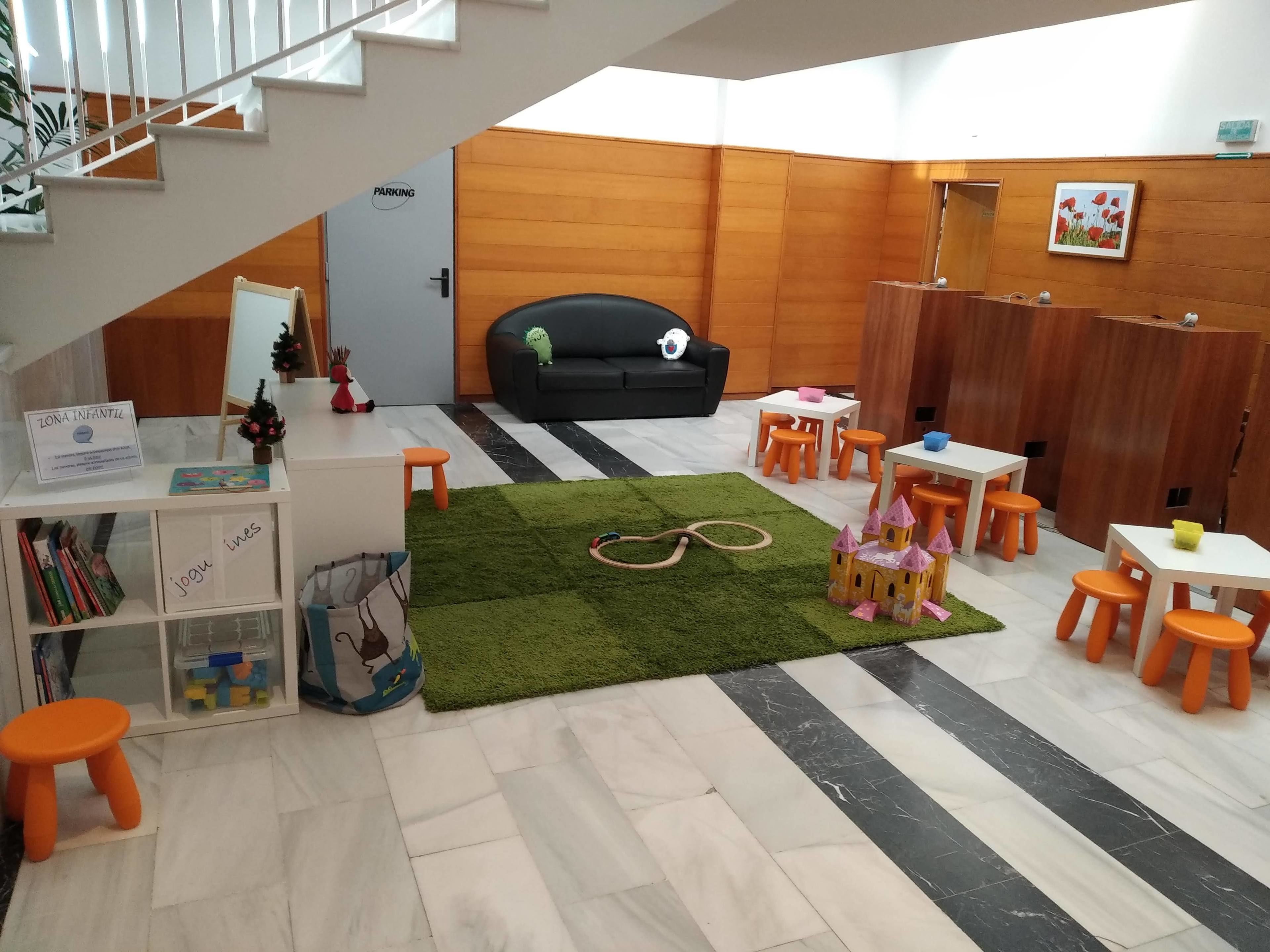 A children's play area with a black couch, orange stools, and a green carpet.