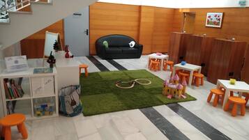 A children's play area with a black couch, orange stools, and a green carpet.
