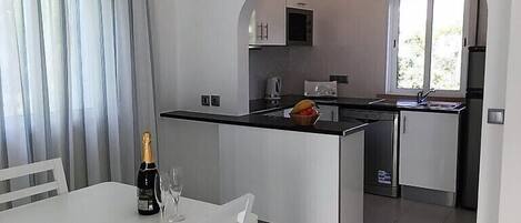 A modern kitchen with an island, a dining area with a table and chairs, and a view of the kitchen through an archway.