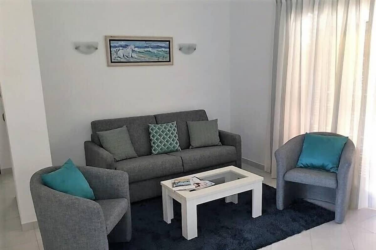 A living room with a grey sofa, two armchairs, a coffee table, and a painting on the wall.