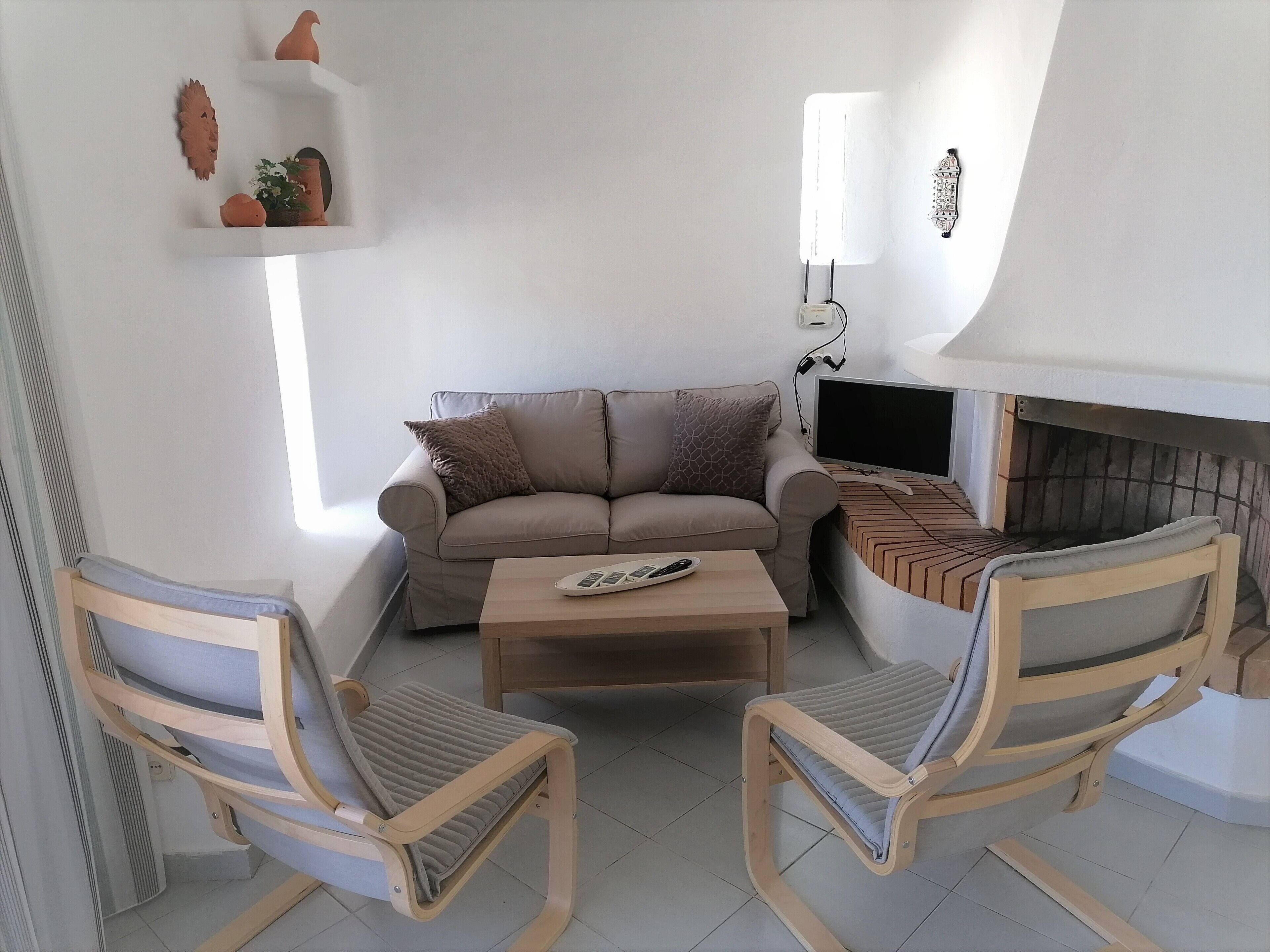 A living room with a beige sofa, two wooden chairs, a coffee table, and a TV.