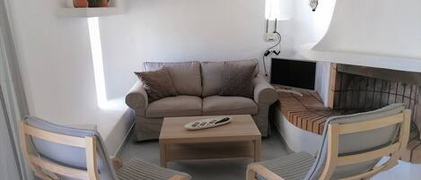 A living room with a beige sofa, two wooden chairs, a coffee table, and a TV.