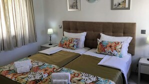 A hotel room with two beds, floral bedspreads, a brown headboard, and two wall-mounted artworks. - Prado do Golf (Loulé)