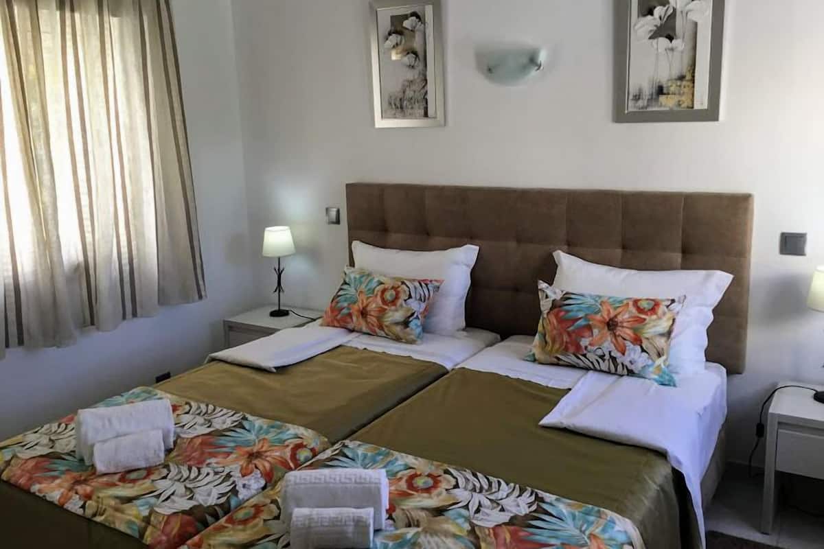 A hotel room with two beds, floral bedspreads, a brown headboard, and two wall-mounted artworks.