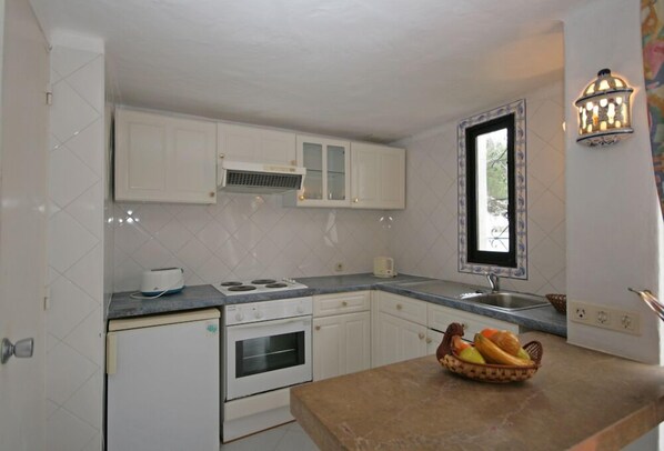 A compact kitchen with white cabinets, a built-in oven, a stove, a sink, and a window with a view. - Prado do Golf (Loulé)