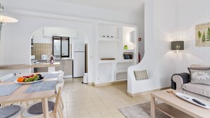 A modern living room with a sofa, a coffee table, and a dining area with a table set for two. - Prado do Golf (Loulé)