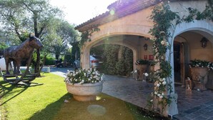 A courtyard with a horse statue, a fountain, and a building entrance with arches and potted plants.
