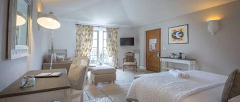 A hotel room with a bed, a desk, a chair, a TV, and a window with curtains.