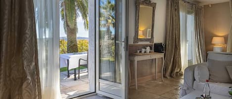 A hotel room with a sliding glass door leading to an outdoor area with a table and chairs, a small desk with a mirror, and a sofa.
