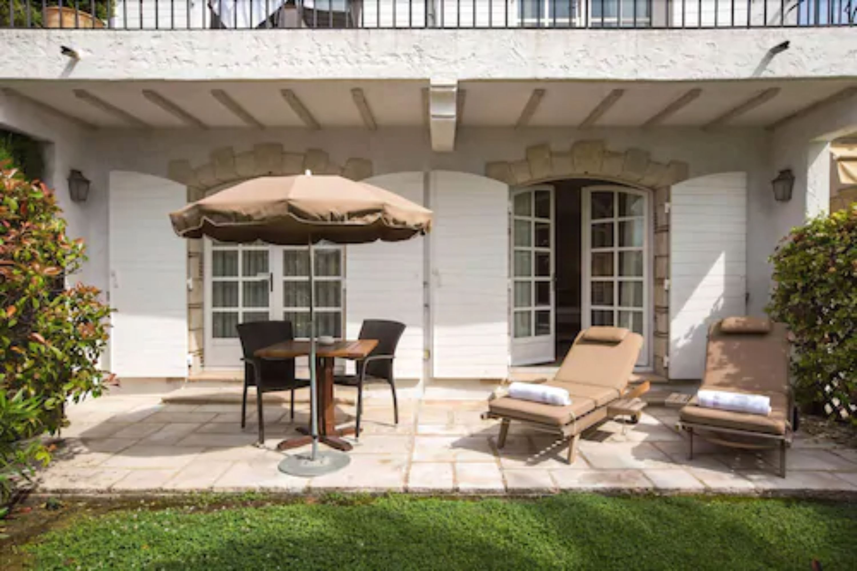 A patio with a table and chairs, a sun lounger, and a covered umbrella.