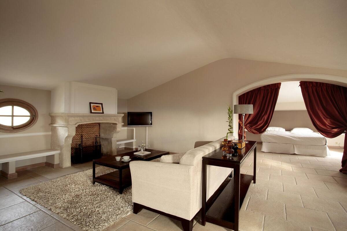 A spacious living room with a fireplace, a television, a sofa, and a bed with red curtains.