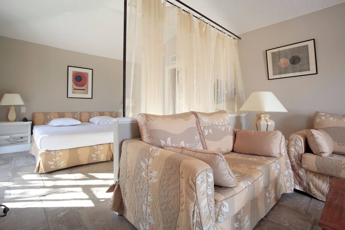 A bedroom with a bed, two sofas, a nightstand, a lamp, and a framed picture on the wall.
