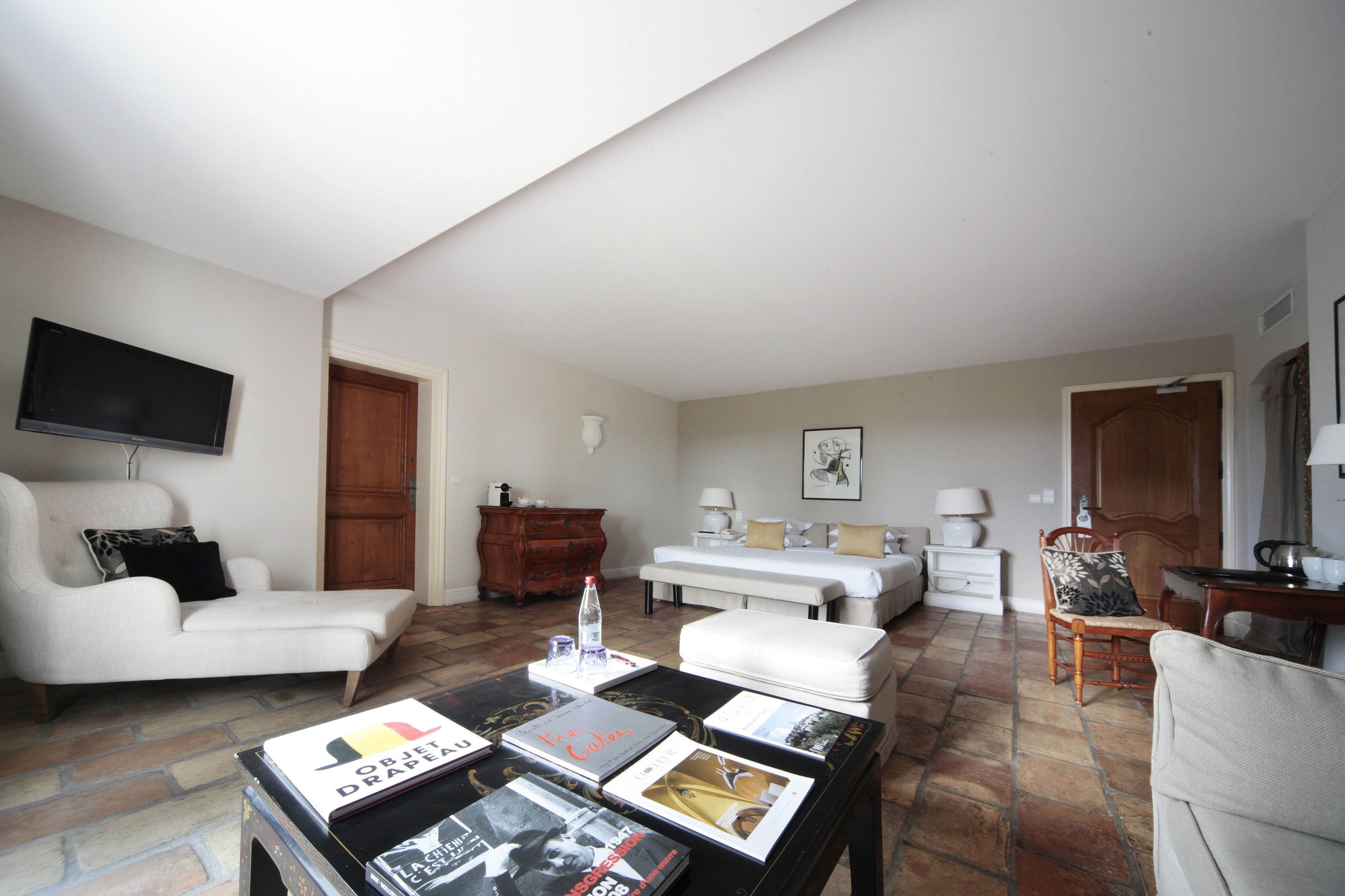 Una sala de estar con un sofá, un sillón, una mesita de centro con revistas, un televisor y una cama al fondo.